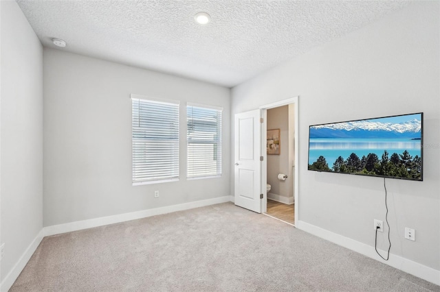 unfurnished bedroom with light carpet, connected bathroom, and a textured ceiling