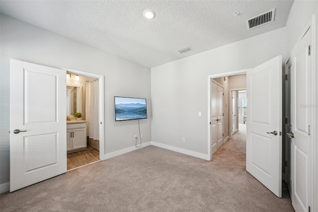 unfurnished bedroom featuring light colored carpet, a textured ceiling, and ensuite bathroom