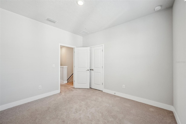 spare room featuring light colored carpet and a textured ceiling