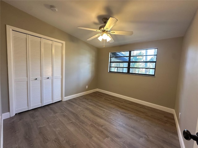 unfurnished bedroom with ceiling fan, a closet, baseboards, and dark wood-type flooring