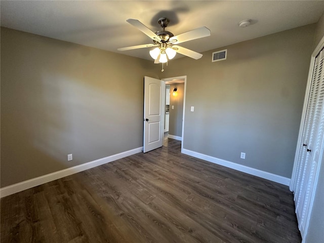 unfurnished bedroom with dark wood-style flooring, a closet, visible vents, ceiling fan, and baseboards