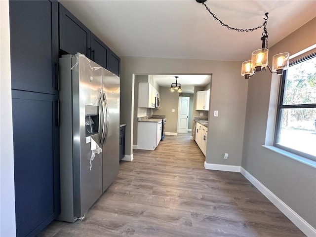 kitchen featuring stainless steel appliances, wood finished floors, white cabinets, baseboards, and pendant lighting