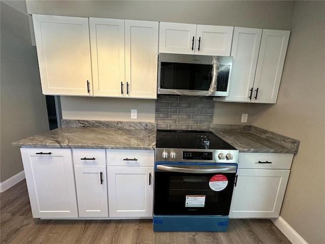 kitchen with stainless steel appliances, dark stone counters, white cabinetry, and dark wood-type flooring