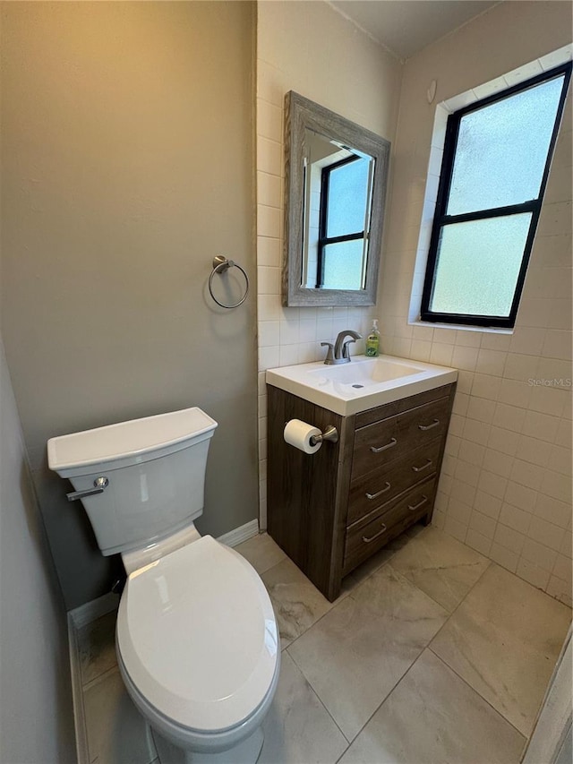 bathroom with marble finish floor, vanity, toilet, and tile walls