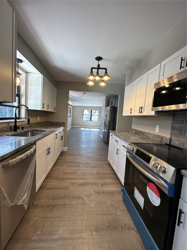 kitchen featuring appliances with stainless steel finishes, white cabinets, a sink, wood finished floors, and dark stone counters