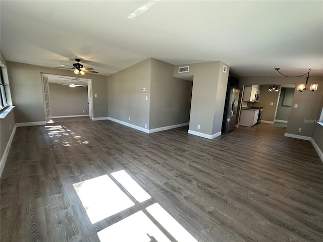 unfurnished living room with ceiling fan with notable chandelier, dark wood-style flooring, visible vents, and baseboards