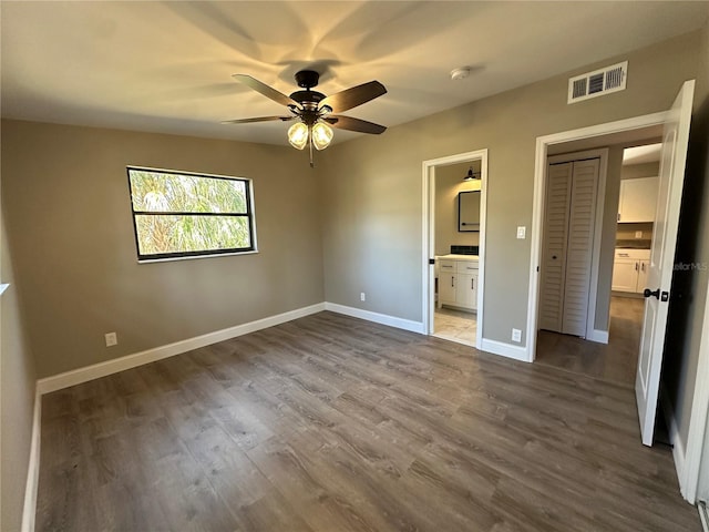 unfurnished bedroom with ensuite bathroom, dark wood-style flooring, a ceiling fan, visible vents, and baseboards