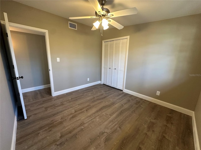 unfurnished bedroom featuring dark wood-style flooring, a closet, visible vents, and baseboards