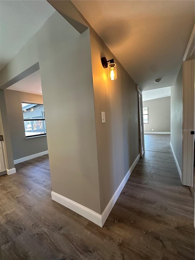 corridor featuring baseboards and dark wood-type flooring