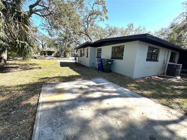 view of side of property featuring cooling unit, a patio area, concrete block siding, and a lawn