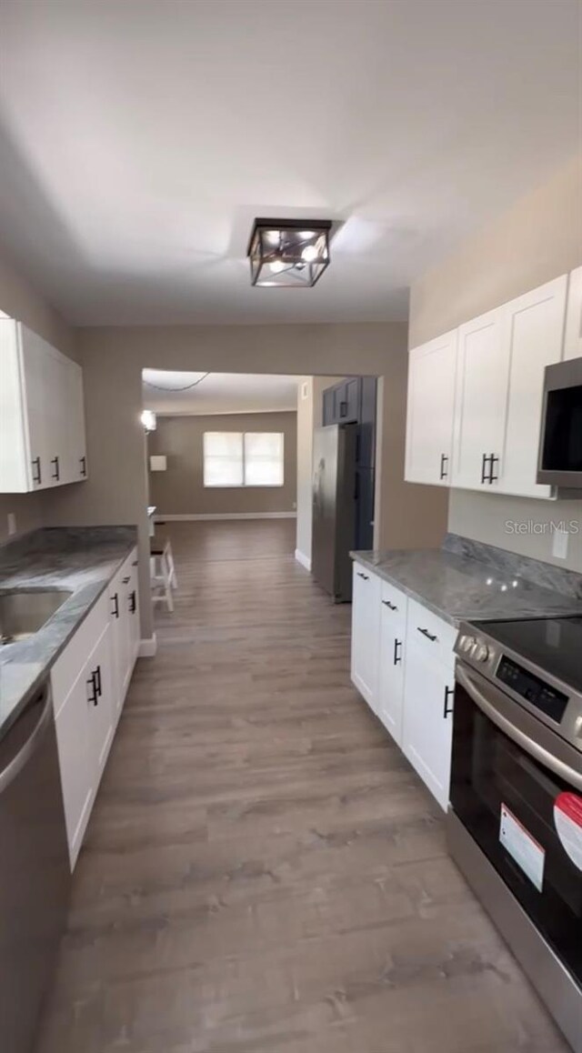 kitchen featuring stainless steel appliances, white cabinets, a sink, wood finished floors, and baseboards
