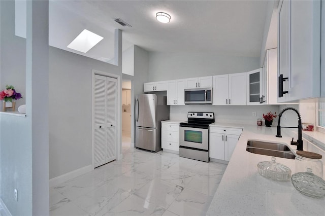 kitchen with sink, appliances with stainless steel finishes, white cabinetry, high vaulted ceiling, and light stone counters