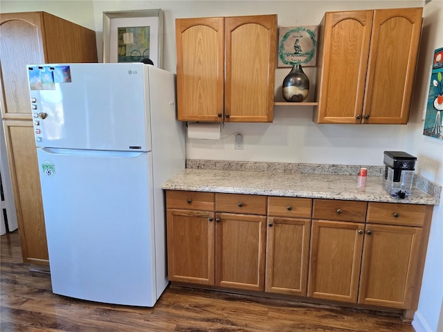 kitchen featuring dark hardwood / wood-style flooring, fridge, and light stone counters