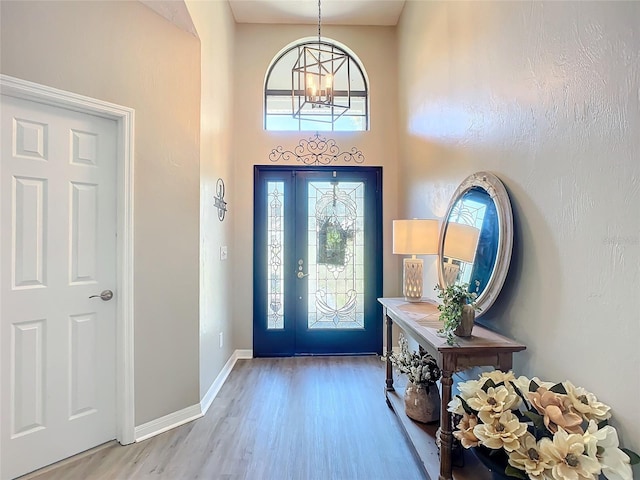 foyer entrance featuring a notable chandelier, a towering ceiling, and light wood-type flooring