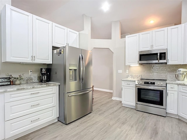 kitchen featuring light stone counters, tasteful backsplash, light wood-type flooring, appliances with stainless steel finishes, and white cabinets