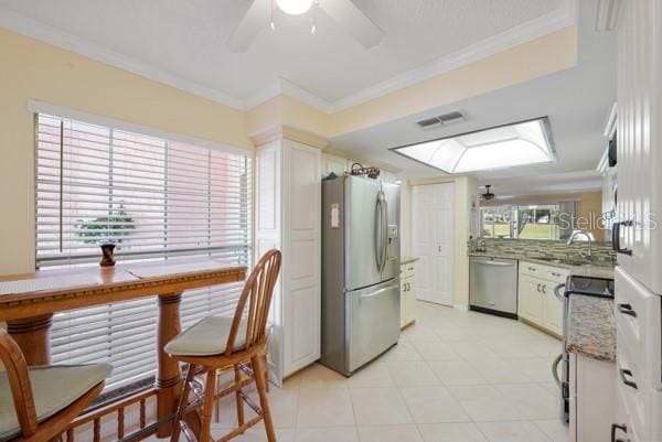 kitchen featuring white cabinetry, appliances with stainless steel finishes, ornamental molding, and a skylight