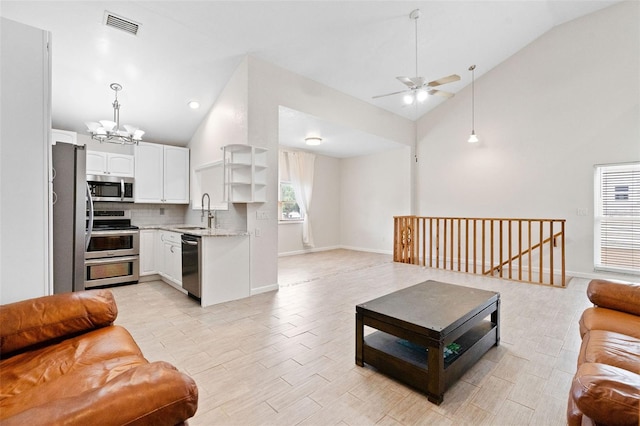 living room featuring ceiling fan with notable chandelier, high vaulted ceiling, light hardwood / wood-style floors, and sink