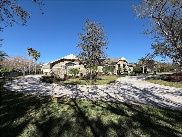 view of front of home featuring stone siding, decorative driveway, a front yard, and stucco siding