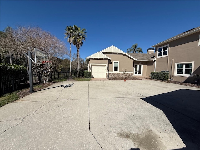 view of side of property featuring a garage, fence, driveway, stone siding, and stucco siding