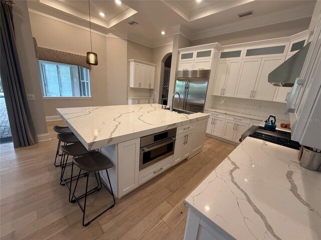 kitchen with light stone counters, decorative light fixtures, a center island with sink, stainless steel appliances, and white cabinetry