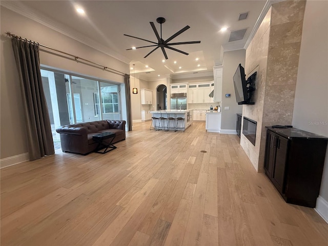 living area with arched walkways, visible vents, light wood finished floors, a tiled fireplace, and crown molding