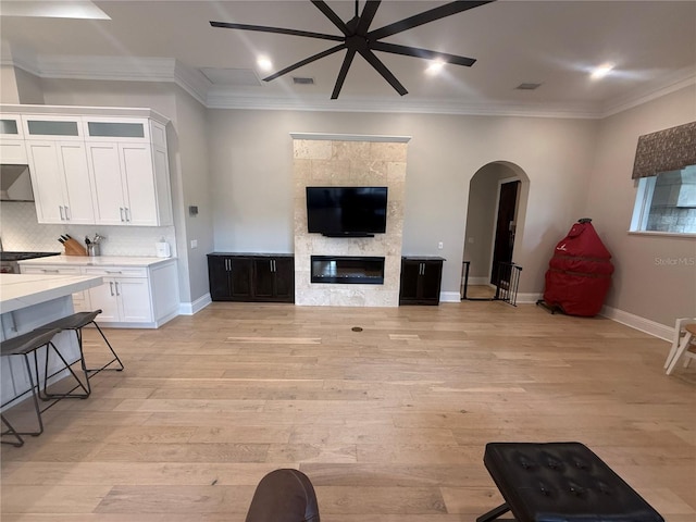 living room featuring light wood-style floors, arched walkways, ornamental molding, and a glass covered fireplace