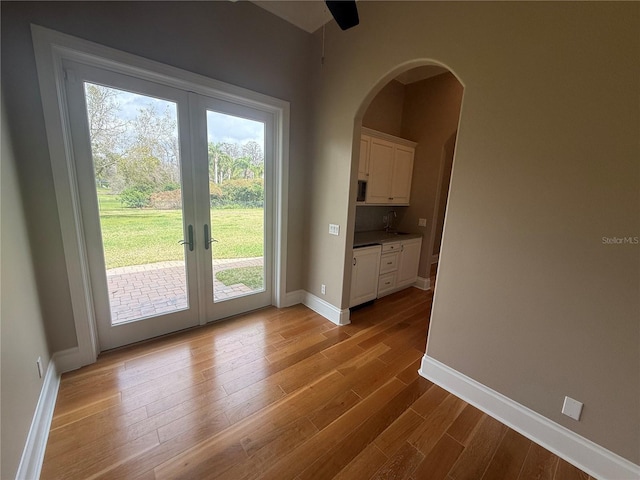 doorway featuring arched walkways, french doors, light wood-style flooring, a sink, and baseboards