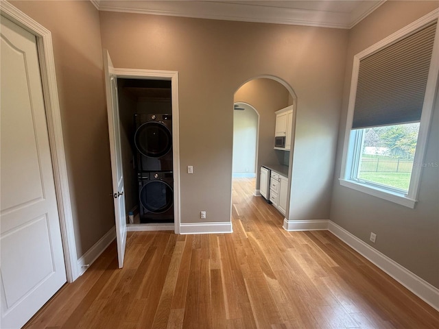 interior space featuring arched walkways, stacked washer / dryer, baseboards, light wood-style floors, and ornamental molding