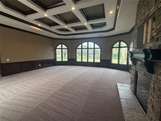 empty room featuring a wealth of natural light, light colored carpet, wainscoting, and a stone fireplace