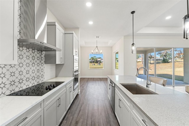 kitchen with stainless steel appliances, light stone countertops, sink, and wall chimney range hood