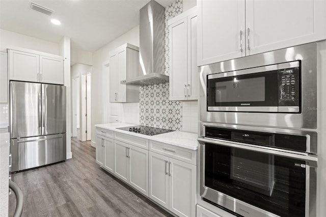 kitchen featuring wall chimney exhaust hood, stainless steel appliances, light stone countertops, and white cabinets