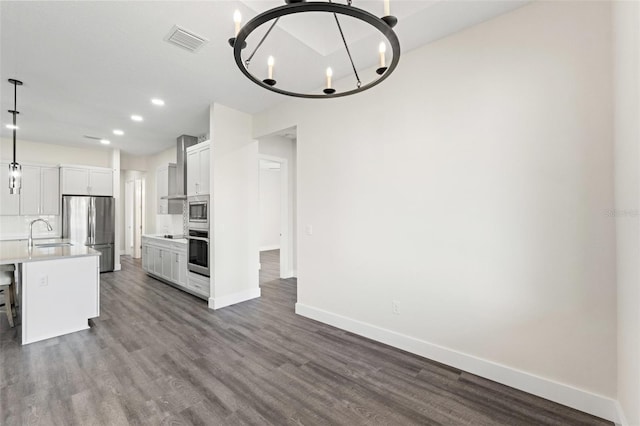 kitchen featuring sink, appliances with stainless steel finishes, a kitchen island with sink, hanging light fixtures, and white cabinets