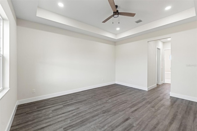 empty room featuring dark hardwood / wood-style flooring, a tray ceiling, and ceiling fan