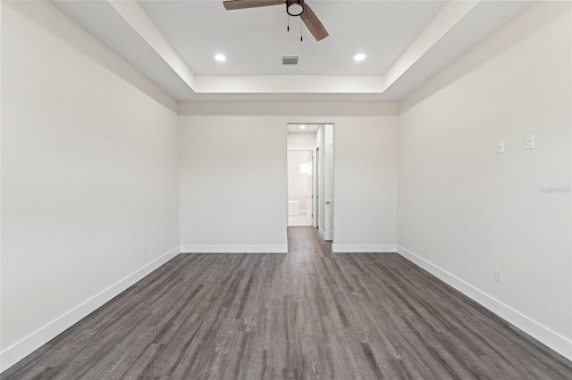 spare room with a tray ceiling, dark wood-type flooring, and ceiling fan