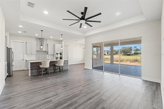 unfurnished living room with dark wood-type flooring, sink, ceiling fan, and a tray ceiling