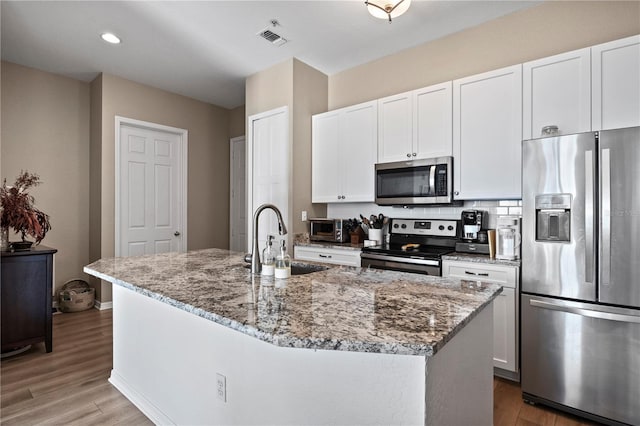 kitchen featuring appliances with stainless steel finishes, an island with sink, sink, white cabinets, and light stone counters