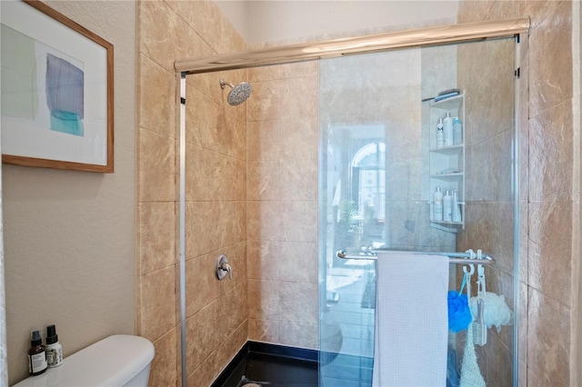 bathroom featuring a shower with door and toilet