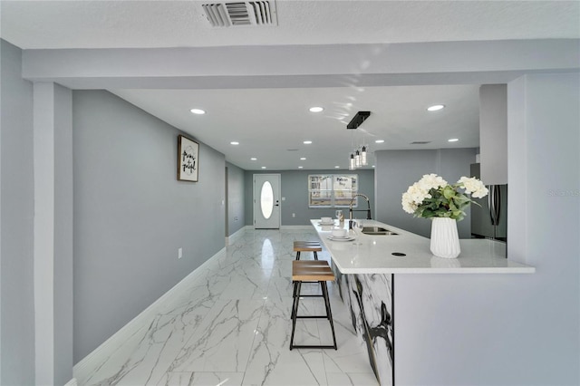 kitchen featuring sink, a breakfast bar area, stainless steel fridge, decorative light fixtures, and kitchen peninsula