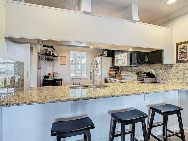 kitchen with sink, white appliances, backsplash, a kitchen bar, and kitchen peninsula