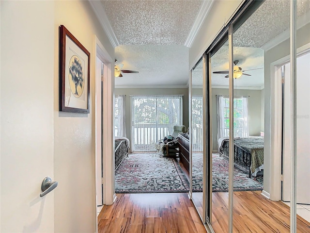 corridor featuring ornamental molding, a textured ceiling, and light wood-type flooring