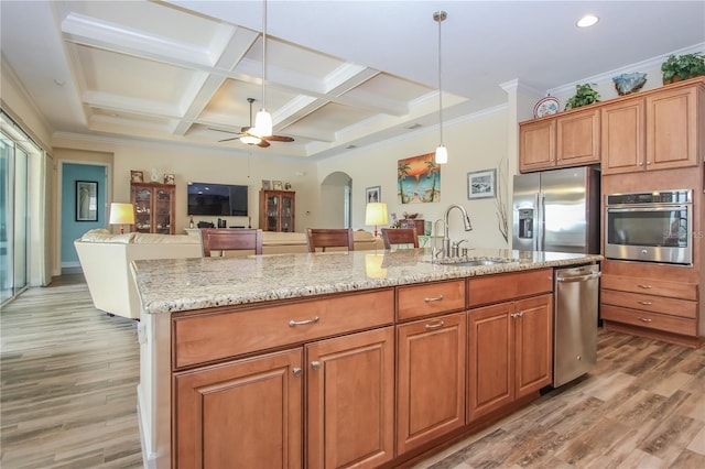 kitchen with coffered ceiling, sink, hanging light fixtures, appliances with stainless steel finishes, and an island with sink