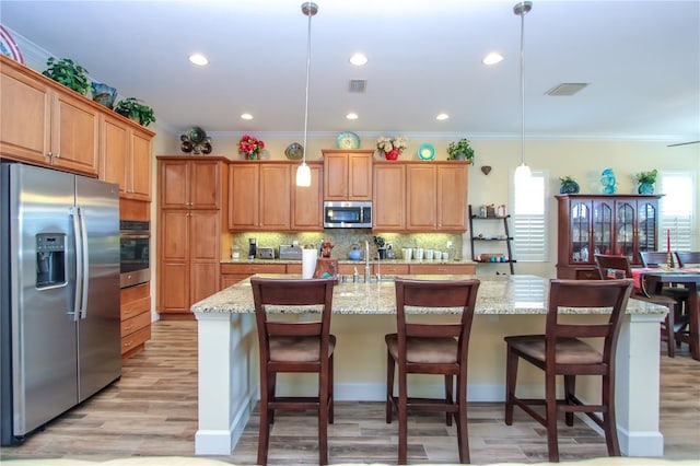 kitchen with pendant lighting, light stone countertops, stainless steel appliances, and a center island with sink