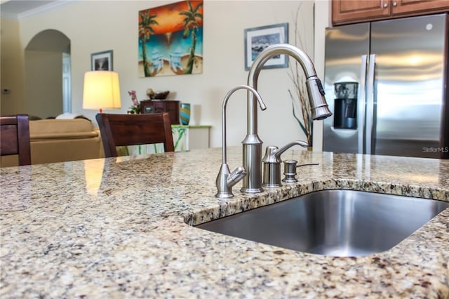 kitchen with stainless steel refrigerator with ice dispenser, crown molding, sink, and light stone counters