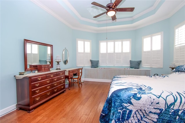 bedroom featuring multiple windows, light hardwood / wood-style floors, and a tray ceiling