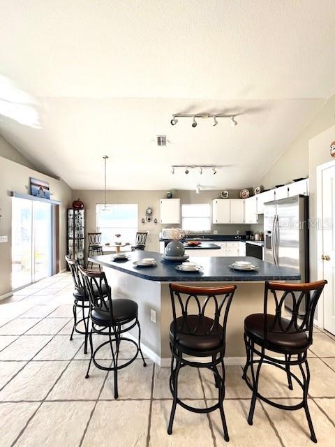 kitchen with a breakfast bar area, white cabinetry, hanging light fixtures, stainless steel refrigerator with ice dispenser, and vaulted ceiling