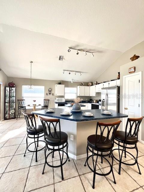 kitchen featuring white cabinetry, hanging light fixtures, a kitchen breakfast bar, stainless steel refrigerator with ice dispenser, and vaulted ceiling