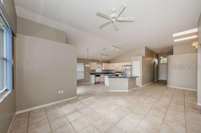 kitchen with pendant lighting, appliances with stainless steel finishes, white cabinets, a kitchen island, and vaulted ceiling