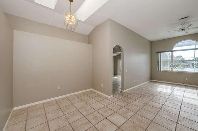 tiled empty room featuring lofted ceiling with skylight and ceiling fan with notable chandelier