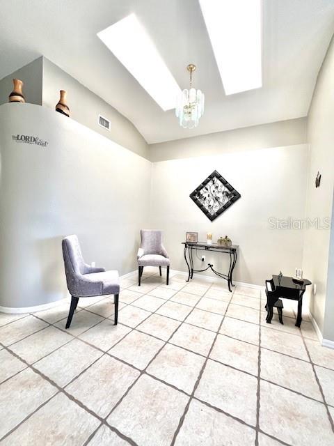 living area with an inviting chandelier, tile patterned floors, and lofted ceiling with skylight