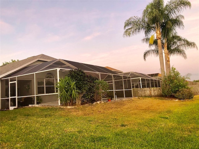 back house at dusk featuring a lanai and a lawn